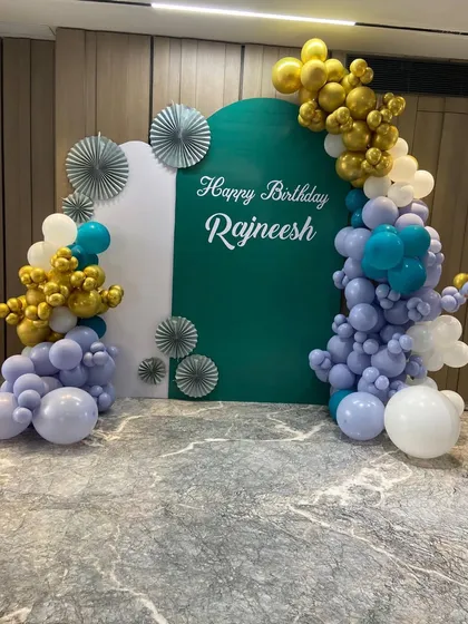 A sophisticated and personalized 50th birthday backdrop. We used custom arched panels in white and deep green, adorned with an organic balloon garland in lavender, teal, and chrome gold for a unique and modern celebration.