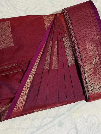 A deep maroon saree with a delicate border, folded with care to maintain its elegance.