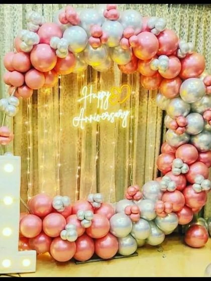 A gorgeous first anniversary photo backdrop. This design includes a circular arch of pink and silver chrome balloons, a 'Happy Anniversary' neon sign, and a light-up number '1'.