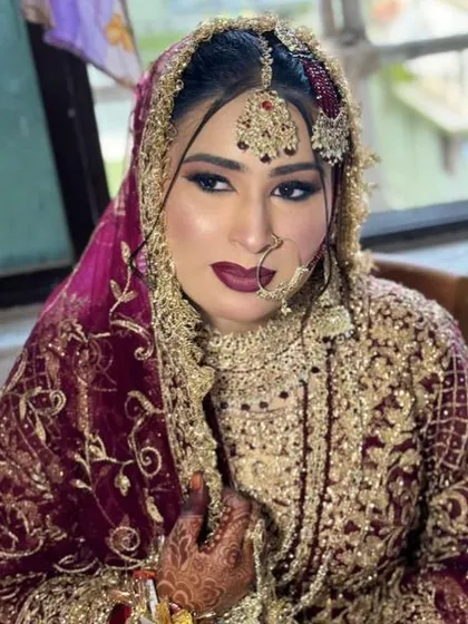 This royal bridal look is all about drama and opulence. The makeup features dark, smoky eyes, a deep maroon lip, and a contoured base to complement the heavy gold and maroon outfit.