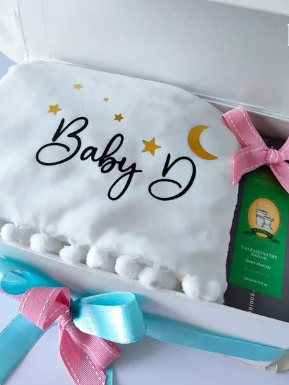 A close-up of the contents inside the cloud hamper, showing the personalized "Baby D" pillow and a gift of luxury tea for the expecting parents.