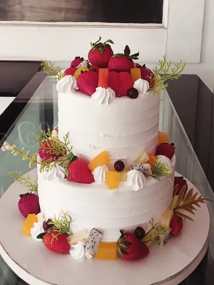 A two-tiered fresh fruit cake, elegantly decorated with strawberries and other seasonal fruits.