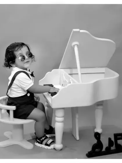 A stylish black and white portrait of a little boy at a miniature piano, giving the photo a classic, old-hollywood feel.