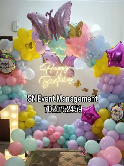 A beautiful pastel butterfly theme for a first birthday. The decoration includes a balloon arch with a large butterfly foil balloon, a light-up number '1', and a neon sign.