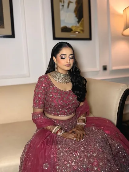 A close-up of a stunning reception bride. The soft glam makeup features a silver-toned smokey eye and a neutral pink lip, which beautifully complements her heavily embellished pink lehenga and silver jewelry.