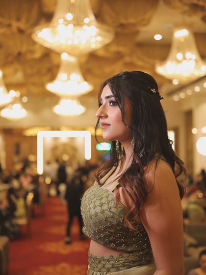 A candid profile shot in a modern olive green draped ethnic outfit. The grand chandeliers in the background add to the luxurious feel.