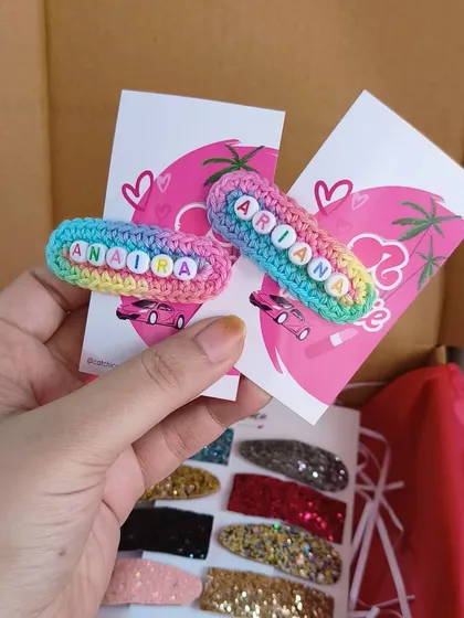 Holding up a pair of custom name clips for 'Anaira' and 'Ariana'. You can see how the colorful beads really pop against the pastel rainbow crochet base.