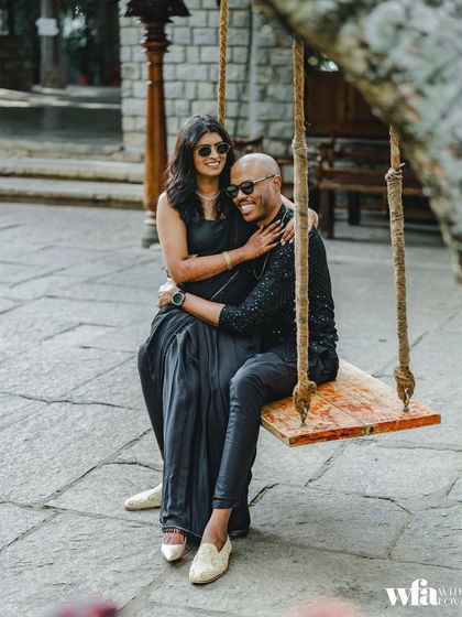 A stylish couple in black outfits shares a laugh on our iconic swing, perfect for a pre-wedding photoshoot.
