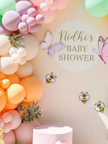 A detailed view of the personalized "Nidhi's Baby Shower" sign, surrounded by pastel balloons and whimsical bee and butterfly accents.