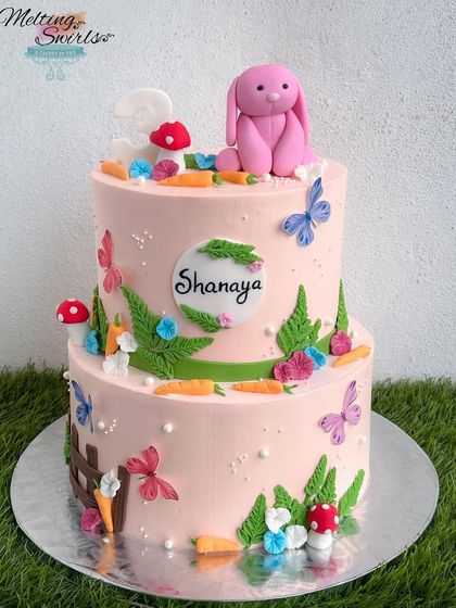 A lovely two-tier garden-themed cake with a cute pink bunny on top. This cake was part of a beautiful party setup, as seen in the client photos.