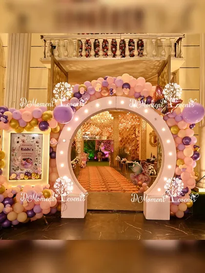 A stunning circular entrance arch for a butterfly-themed first birthday. The arch is adorned with pastel purple and peach balloons, gold accents, and a custom welcome sign, creating an elegant and inviting entryway.