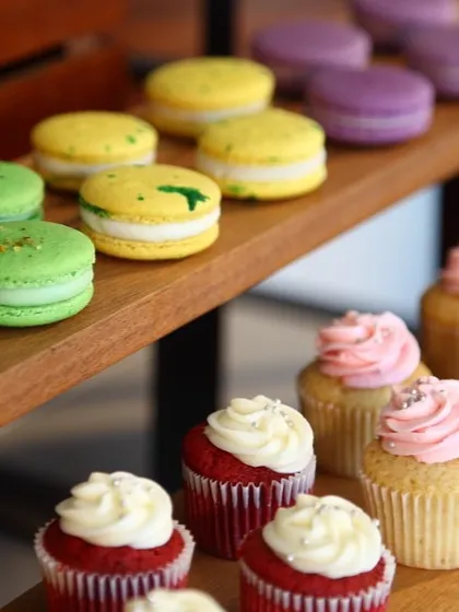 A vibrant display of macarons and cupcakes on a wooden stand. This image captures the colour and variety of our small dessert offerings, perfect for any celebration.