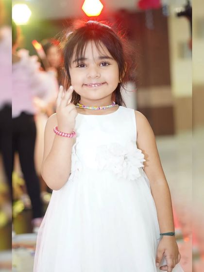 A sweet portrait of a young girl in a white dress, smiling and posing for the camera.