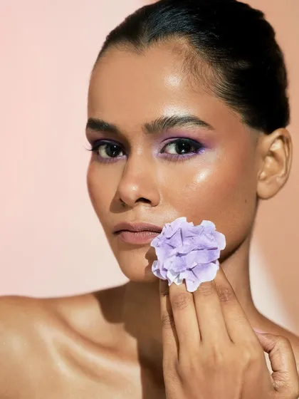 A powerful portrait where the model holds the flower. The vibrant purple on the eyes stands out beautifully against her glowing skin.
