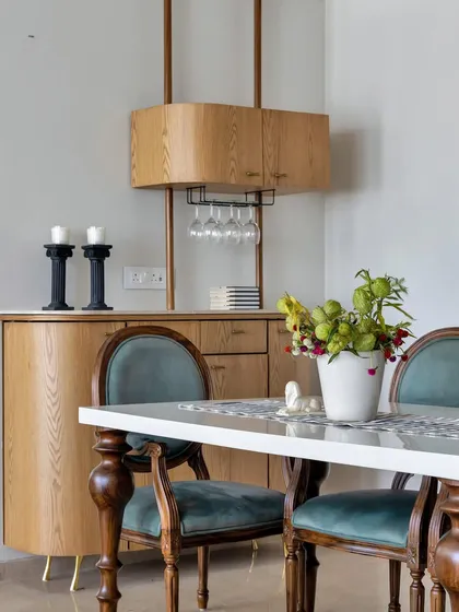A sophisticated cocktail bar is the ideal haven for connoisseurs and casual drinkers alike. This setup features a light wood cabinet with classic turned-leg chairs in a rich teal velvet.