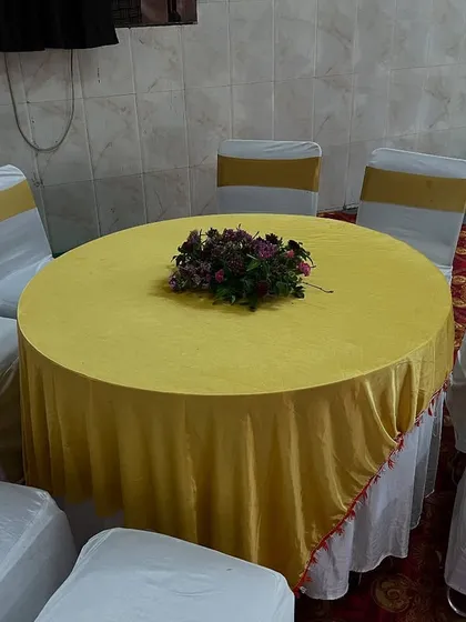 A simple and clean seating arrangement with a yellow tablecloth and white chair covers with gold sashes, ideal for Haldi or Mehendi functions.
