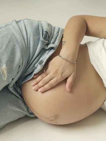 A close up shot focusing on the beautiful baby bump, with the mom's hand resting gently. The casual denim adds a modern, relaxed feel to this intimate photo.