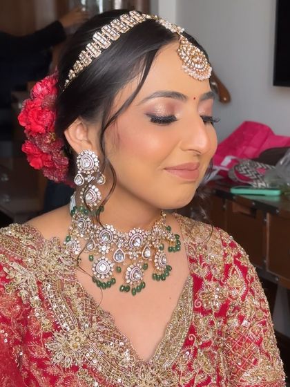 The bride's frontal look, with soft tendrils framing her face and the red floral bun visible from the side.