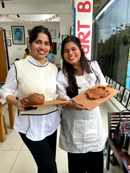 Two friends proudly hold up the clay teapot and tray they made. The workshop allows you to create complex and beautiful pieces with guided instruction.