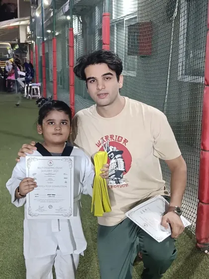 A young student proudly shows off her new yellow belt and certificate. The first step on the ladder is complete.
