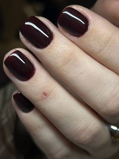 A close-up of a flawless, glossy burgundy manicure. The light reflection shows the perfectly smooth surface achieved with our techniques.