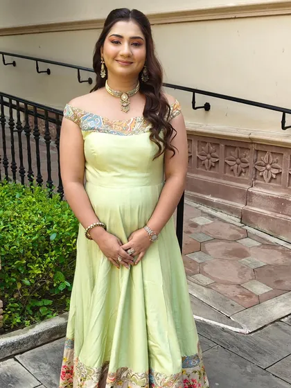 A fresh and glowing look for a wedding guest at ITC Grand Bharat. Her hair is styled in soft, open waves that match the flowy silhouette of her light green anarkali.