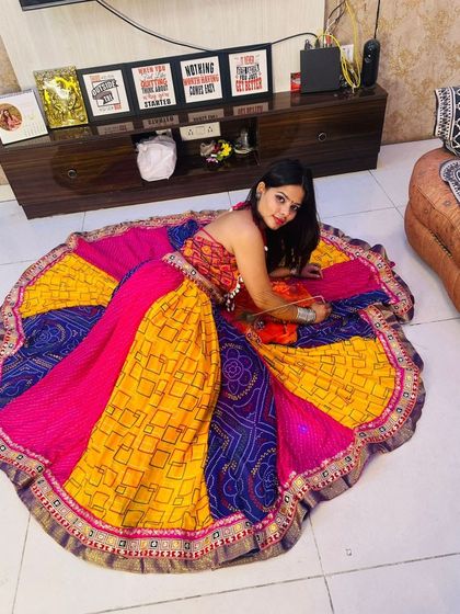 A model posing with her colorful patchwork Garba lehenga spread around her, showcasing the entire design.