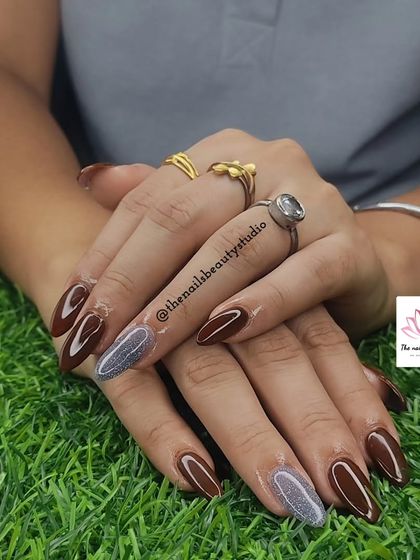 A beautiful set of long, almond-shaped nails with a mix of chocolate brown and a sparkling silver-gray polish.