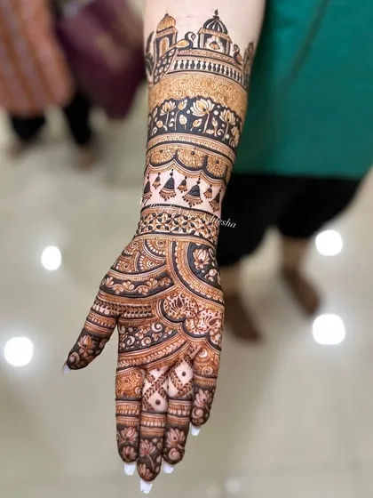 A close-up of a bridal arm design, showcasing a detailed palace motif. The combination of bold outlines and fine shading creates a stunning architectural element in the mehendi.