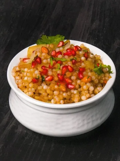 Sabudana khichdi topped with vibrant pomegranate seeds, adding a pop of color and freshness. The dark background makes the colors and textures of the dish stand out.