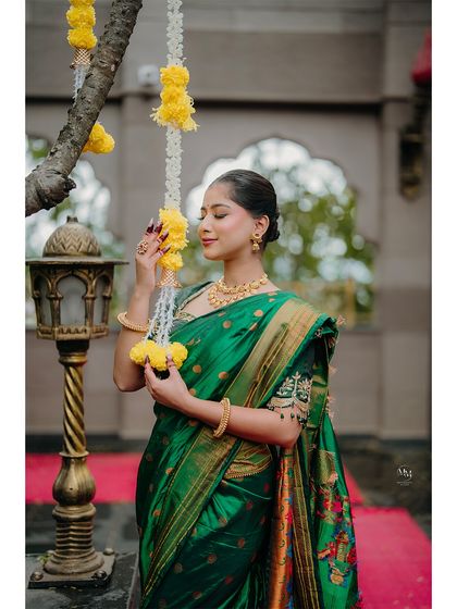 A graceful pose with traditional flower decorations. The bride's emerald green saree and gold jewelry shine in this elegant solo shot.