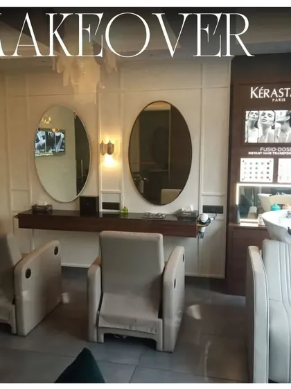 A makeover station within the salon, featuring elegant oval mirrors and integrated brand displays. The clean white paneling and comfortable seating create a bright and professional space for beauty transformations.