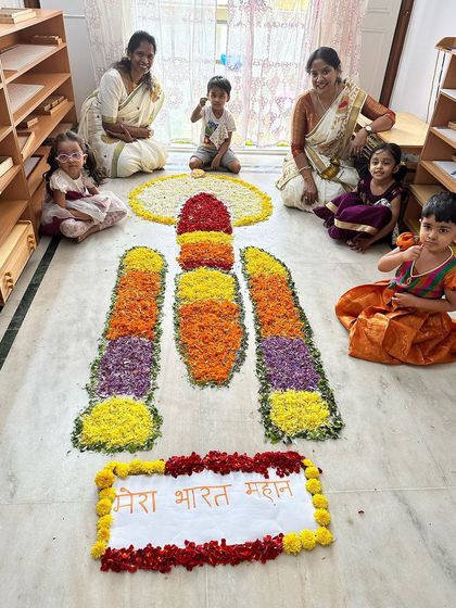 Our children, dressed in beautiful festive clothes, proudly pose with the Chandrayaan-themed flower rangoli they helped create for Onam.