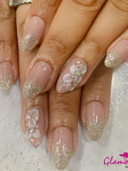 The perfect combination of sparkle and floral. This elegant set features a glittery French tip on a nude base, with accent nails adorned with a cascade of delicate, 3D mother-of-pearl flowers.