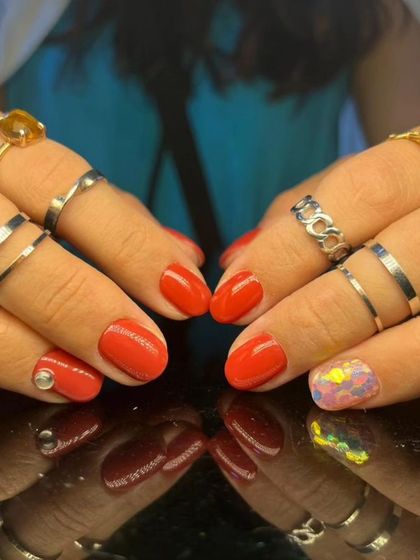 A full view of the bright red manicure with the playful confetti accent.