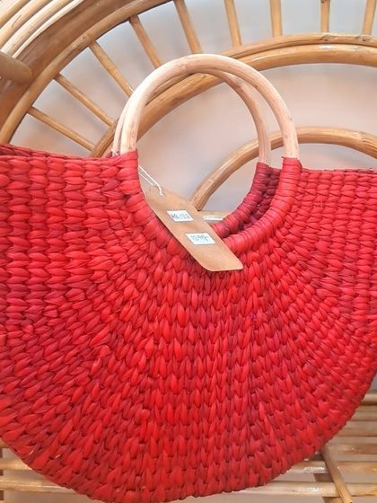 A bold and beautiful red woven handbag with a natural wood handle, resting on a cane chair. This image highlights how we use vibrant colors to bring a modern twist to traditional, sustainable materials.