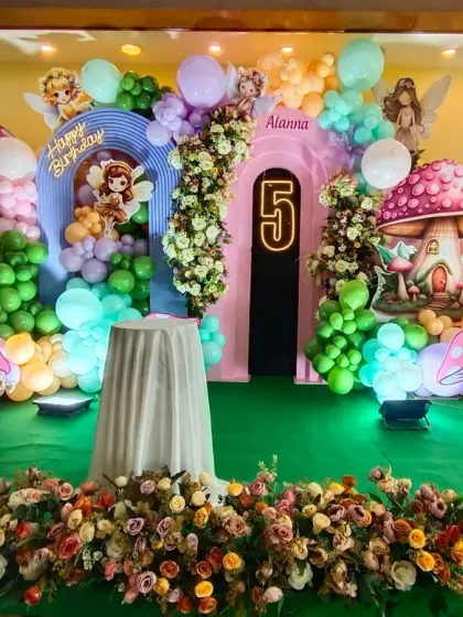 An enchanted forest theme for a 5th birthday party. The stage is decorated with magical mushroom props, fairy cutouts, and a lush arrangement of balloons and flowers, creating a storybook setting.