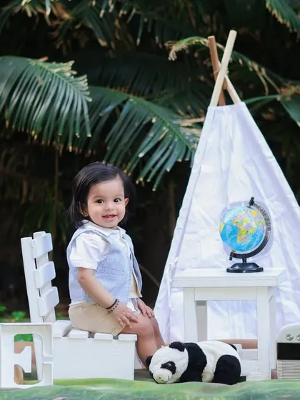 An outdoor first birthday shoot with a travel theme. This little boy is sitting in front of a teepee with a globe and vintage camera props.