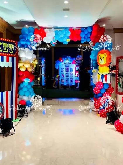 The entrance to a Carnival-themed party, complete with a "TICKET" booth prop and a colorful balloon arch. A lion character cutout adds to the fun circus atmosphere.