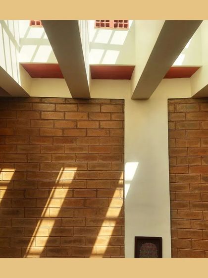 Beams of sunlight stream in from high clerestory windows, creating strong diagonal lines across an exposed brick wall. This technique allows for natural illumination while maintaining privacy in the spaces below.