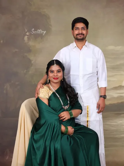 A classic studio portrait of a couple in traditional South Indian attire. Their formal pose and the painterly backdrop give the image a timeless and elegant quality.