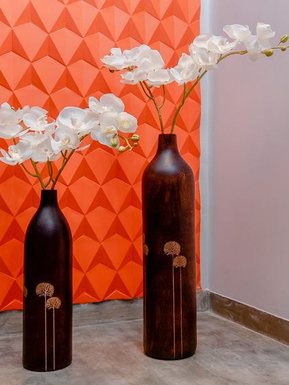 The repetition of the white orchid flowers in dark wooden vases against a geometric orange wall creates a pleasing and rhythmic decorative pattern.