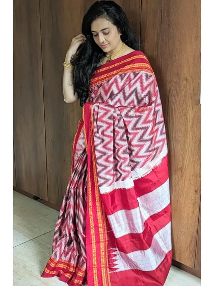 A full-length shot of the red and white Ikat saree. The combination of the intricate body pattern and the simple striped pallu is perfectly balanced.