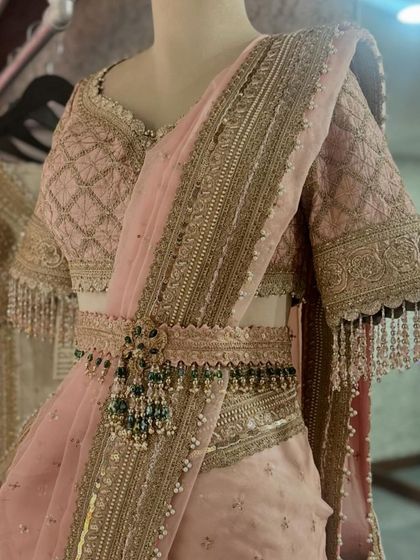A close-up of a beautiful pink saree by Shikhar Sharma, featuring a heavily embroidered blouse and a statement belt with green bead drops.