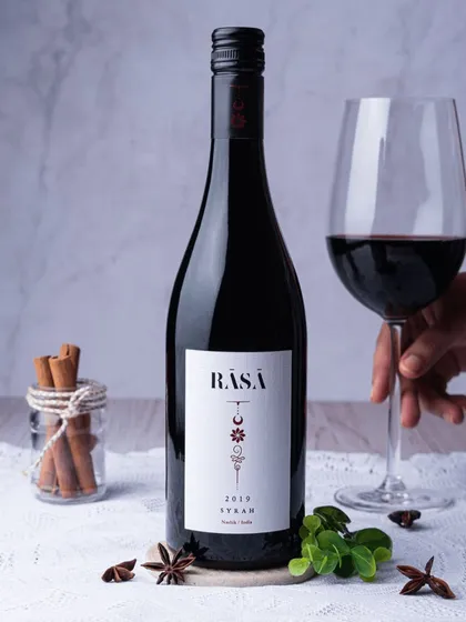 This shot of red wine is styled with spices like cinnamon and star anise, hinting at its flavor profile. The clean, light background provides a nice contrast to the dark bottle and rich color of the wine.