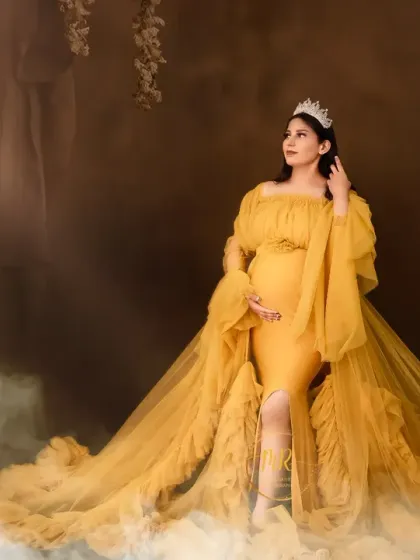 A majestic maternity portrait in a flowing yellow gown and crown. The addition of floor mist creates a dreamy, ethereal atmosphere for this studio pregnancy photoshoot.