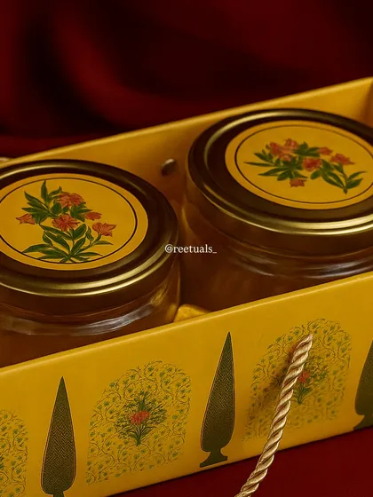 Simplicity can be so beautiful. This close-up shows two glass jars with floral-printed lids, nestled in a festive yellow gift bag. It's a perfect example of a minimal yet thoughtful dry fruit gift for Diwali.