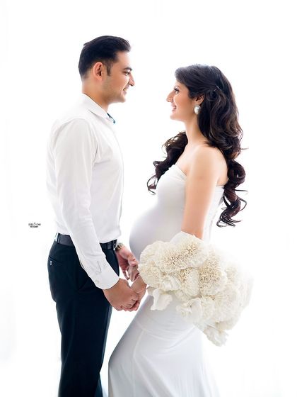 A classic couple's pose in an all-white theme. The couple's happy expressions and the mother's beautiful gown make for a timeless and elegant maternity photo.