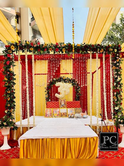 The main stage for the Kirtan ceremony. The seating area is framed by a floral arch and a backdrop of hanging flower strings, creating a beautiful and divine focal point.