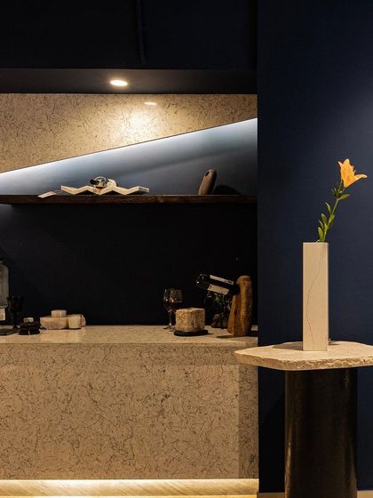 Every corner is an opportunity for a design moment. A simple stone pedestal table stands against the deep blue wall, its raw texture contrasting with the smooth finish of the wall and the delicate flower it holds.